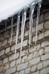 Dangerous icicles in a house roof. Icicles hanging from roof. Icicles on winter nature.
