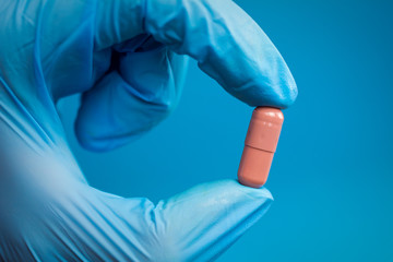  holding a pill with fingers in blue gloves.  painkillers and drug abuse prescription drugs concept.