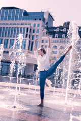 Dancing position. Beautiful female dancer standing in the fountain while holding her hands up © Viacheslav Yakobchuk