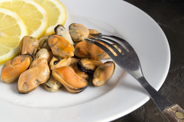 Mussels boiled on a white plate with lemon.