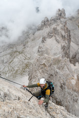 young male climber on a steep and exposed rock face climbing a Via Ferrata