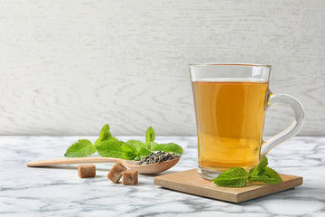 Cup of hot aromatic mint tea and spoon with dry leaves on marble table