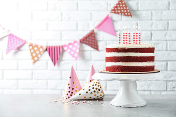 Fototapeta premium Delicious homemade red velvet cake with candles on table against brick wall. Space for text