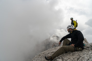 young male mountain climber on a Dolomite mountain peak enjoying the view with his guide standing...