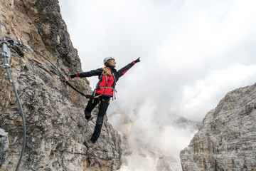 young attractive female university student on a vertical and exposed rock face climbs a Via Ferrata...