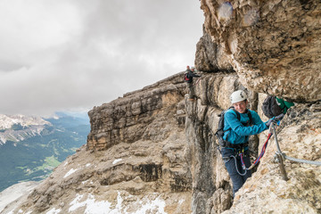 group of young mountain climbers on a steep Via Ferrata with a view of the Italian Dolomites in Alta Badia behind them
