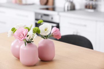 Vases with beautiful flowers on table in kitchen interior. Space for text