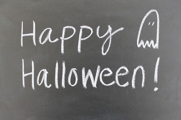 Obraz premium Happy Halloween handwritten on a blackboard with a ghost doodle.
