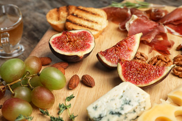 Wooden board with ripe figs and delicious products, closeup