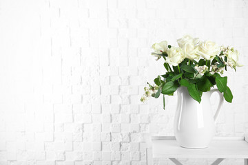 Vase with bouquet of beautiful flowers on table near brick wall. Space for text