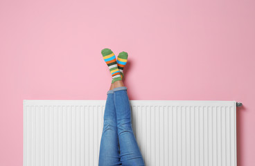 Fototapeta premium Woman warming legs on heating radiator near color wall