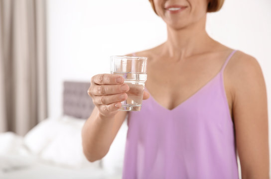 Woman holding glass with clean water in bedroom, closeup. Space for text