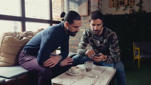 Friends looking at mobile phone and talking in a cafe