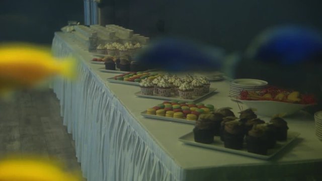Golden fish in a freshwater aquarium slowmotion, cupcakes and desserts at background