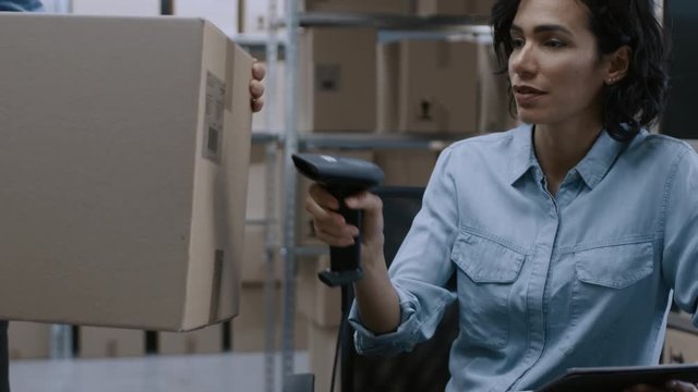 Female Inventory Manager Scans Cardboard Box with Barcode Scanner, Worker Puts Package on the Designated Shelf. In the Background Rows of Cardboard Boxes with Products Ready For Shipment.