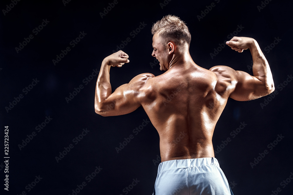 Wall mural handsome strong bodybuilder posing in studio on black background