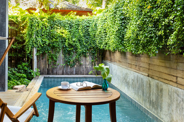 Cup of coffee and glasses on open book on table with green plant in background.