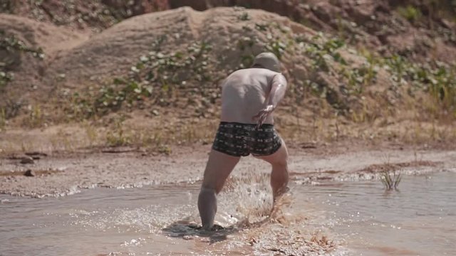 Funny guy in a gas mask and shorts running on a dirty puddle. Guy having fun.