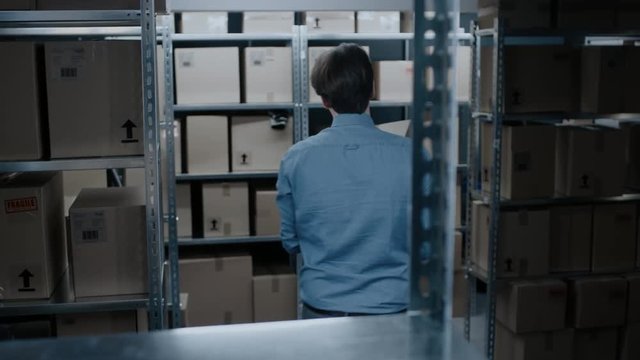 Warehouse Worker Takes Cardboard Box of a Shelf. In the Background, Rows of Shelves Full of Cardboard Boxes and Parcels Filled with Products Ready for Shipment. 