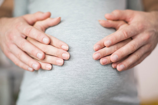 Close Up Of Male And Female Hands Resting On Pregnant Womans Stomach