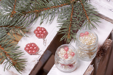 Blue spruce branches on a wooden box of boards, painted in white. Nearby there are earrings and...