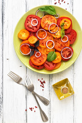 Sliced yellow and red tomatoes with onions and basil in a plate on a white wooden woody table. Top view, flat lay.