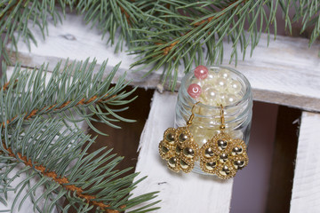 Blue spruce branches on a wooden box of boards, painted in white. Nearby there are earrings and there are jars with beads.