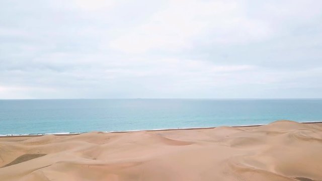 Down up aerial footage of magnificent landscape of sand desert, blue ocean and cloudy sky. Horizon view. Gran Canaria.