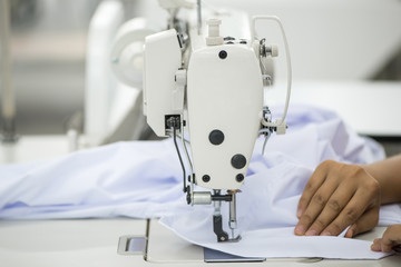 seamstress on a sewing machine makes a shirt in the sewing workshop. the woman on the machine sews the collar and cuffs