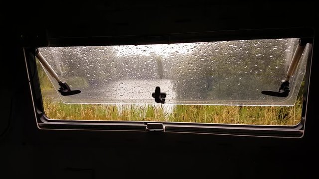 Pouring rain seen through an open motorhome caravan window.