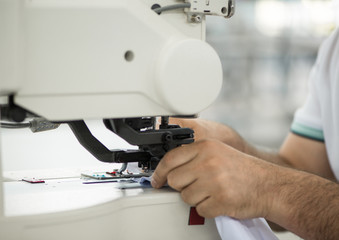 seamstress male on a sewing machine makes a shirt in the sewing workshop. the man on the machine sews the collar and cuffs
