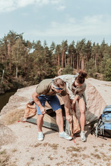 Helpful girlfriend. Dark-haired stylish girlfriend helping her handsome blonde-haired man putting up a tent near beautiful lake