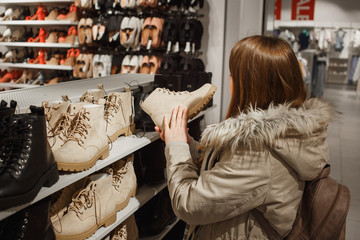 Fototapeta na wymiar Pretty caucasian woman in winter clothes choosing trendy winter boots in the mall