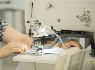 seamstress on a sewing machine makes a shirt in the sewing workshop. the woman on the machine sews the collar and cuffs