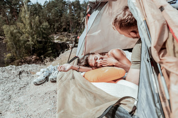Yawning hiker. Dark-haired female hiker wearing bracelet on her hand yawning while feeling tired lying in tent with boyfriend