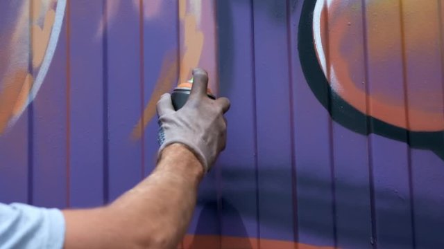 A young guy with a can of paint draws graffiti on the wall. One hand close-up. Slow motion