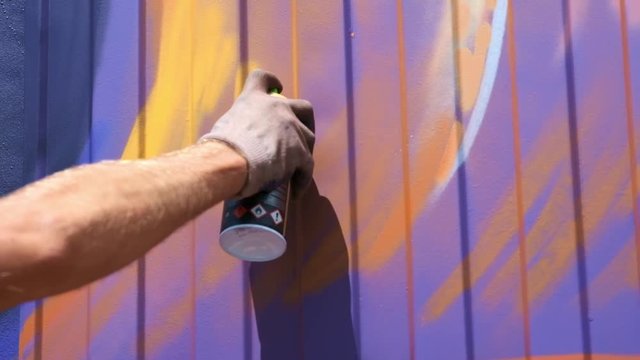 A young guy with a can of paint draws graffiti on the wall. One hand close-up. Slow motion