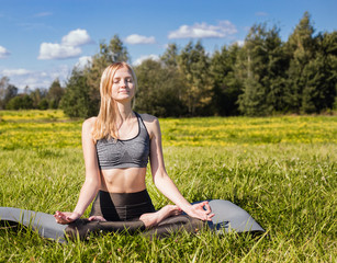 Young female with open arms and long blond hair relaxes in yoga pose in green nature