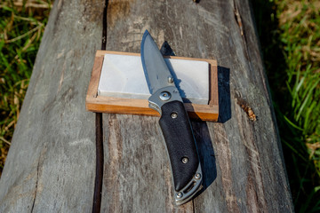 Sharp knife and grindstone on a wooden background.