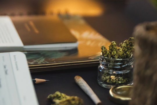 Jar of cannabis buds, gold lid, notebooks, joint on black background