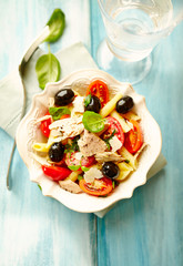 Pasta with tuna, cherry tomatoes, black olives, spices and fresh basil. Home made food. Concept for a tasty and healthy meal. Bright wooden background. Top view. 