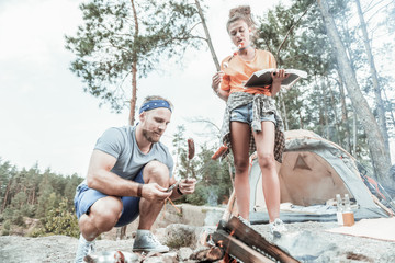 Man cooking. Bearded handsome blonde-haired man cooking sausages for himself and vegetables for his girlfriend