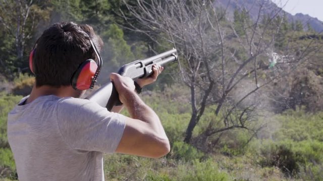 Man firing a shotgun at a target in nature outdoors