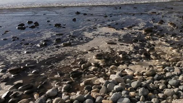 Waves lapping the shore with pebbles and sea foam.