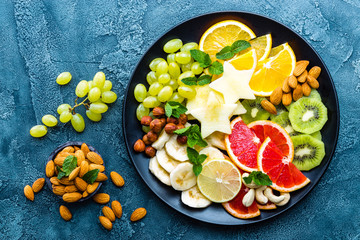 Healthy vegetarian bowl dish with fresh fruits and nuts. Plate with raw apple, orange, grapefruit, banana, kiwi, lemon, grape, almond, hazelnut and cashew nuts. Healthy balanced eating