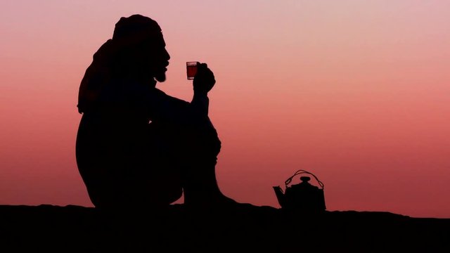 Loop of A Bedouin man pours tea in silhouette against the sunset. Loop 1 of 3.