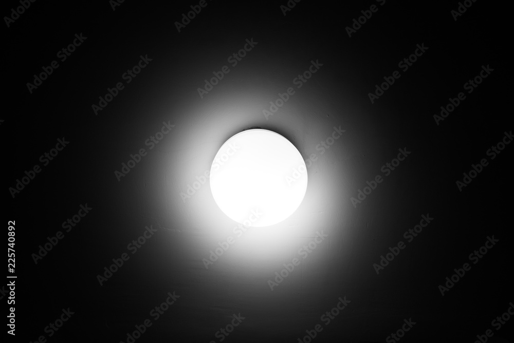 Wall mural Bright lamp on the ceiling in dark room black and white minimalistic image