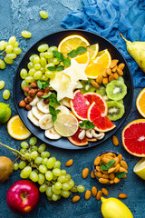 Healthy vegetarian bowl dish with fresh fruits and nuts. Plate with raw apple, orange, grapefruit, banana, kiwi, lemon, grape, almond, hazelnut and cashew nuts. Healthy balanced eating