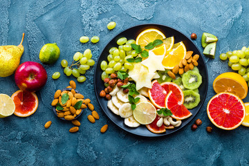 Healthy vegetarian bowl dish with fresh fruits and nuts. Plate with raw apple, orange, grapefruit, banana, kiwi, lemon, grape, almond, hazelnut and cashew nuts. Healthy balanced eating