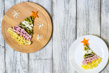 Christmas tree from a salad olivier in plate on a white wooden table. Top view with a copy space